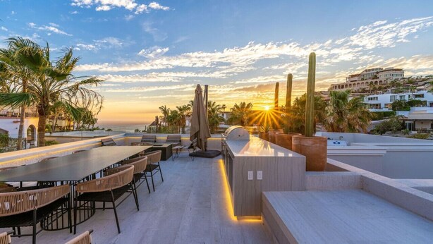 An outdoor dining area with a view of the sunset, palm trees, and a building in the background.