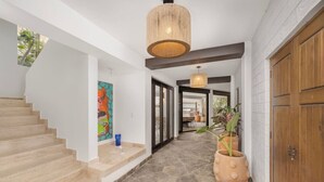 A hallway with a staircase, a hanging light fixture, and potted plants.
