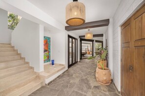 A hallway with a staircase, a hanging light fixture, and potted plants.