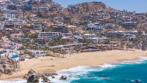 A coastal town with buildings on a hillside, a sandy beach, and the ocean.
