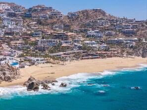 A coastal town with buildings on a hillside, a sandy beach, and the ocean.