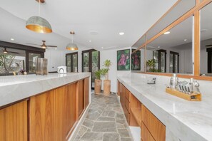 A modern kitchen with a stone floor, wooden cabinets, a marble countertop, and pendant lighting.
