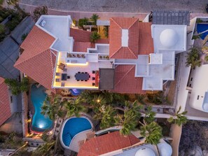A rooftop pool area with a dining setup, surrounded by palm trees and a swimming pool. - Casa La Mexicana @ Pedregal Cabos (Cabo San Lucas)