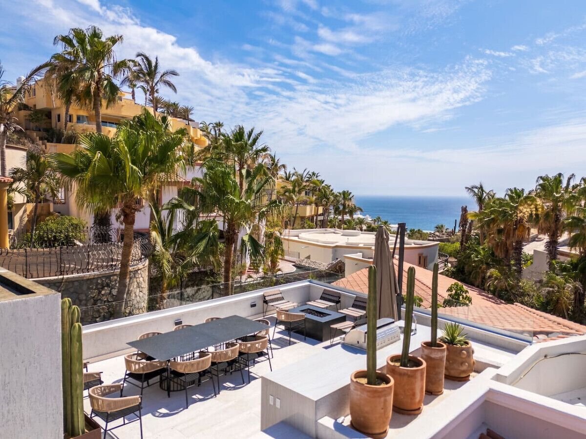 A rooftop terrace with outdoor seating, palm trees, and a view of the sea.