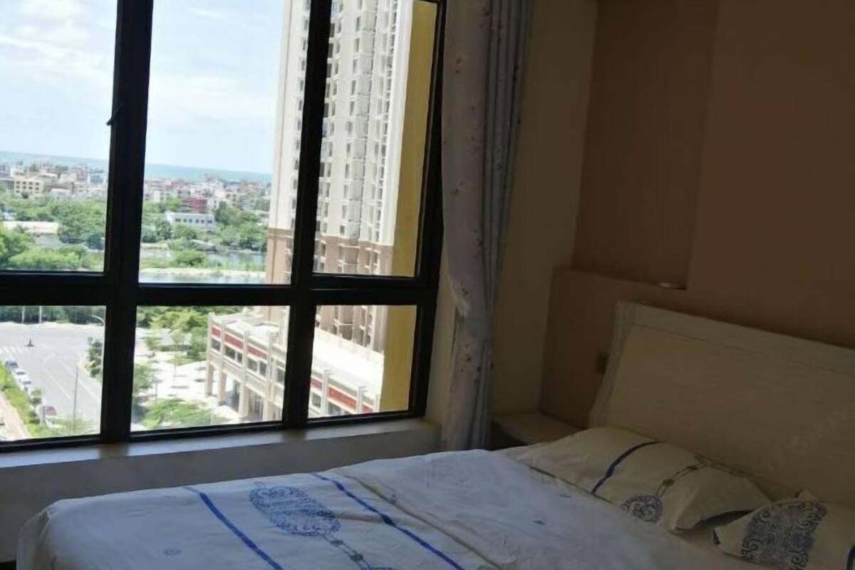 A hotel room with a large window, a bed with a patterned bedspread, and a view of a cityscape.