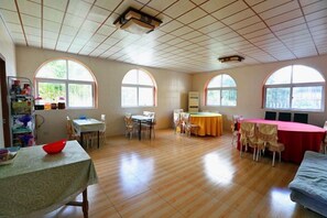 A spacious room with a wooden floor, a dining table, chairs, a sofa, and large arched windows.