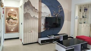 A modern living room with a large TV, a red sofa, and a decorative wall with a circular design. - Youtian Yangsheng Holiday Apartment (Beihai)