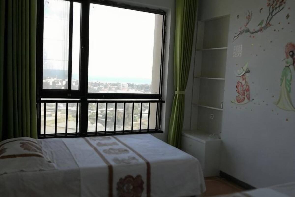A bedroom with a bed, a window with a view, and a wall with artwork.
