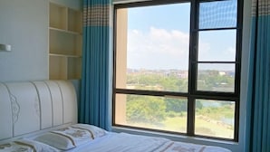 A bedroom with a large window, a bed, and a built-in shelf unit. - Youtian Yangsheng Holiday Apartment (Beihai)