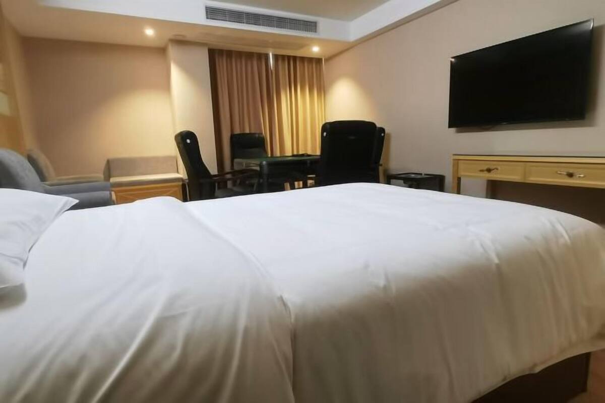Habitación de hotel con cama, escritorio, dos sillas, televisor y ventana con cortinas.