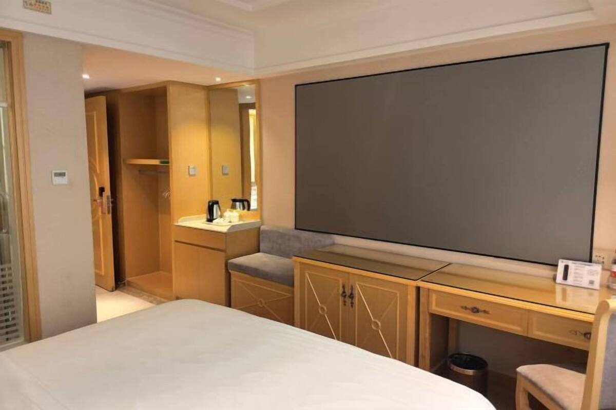 Habitación de hotel con cama, escritorio, silla, un espejo grande y televisor de pantalla plana.