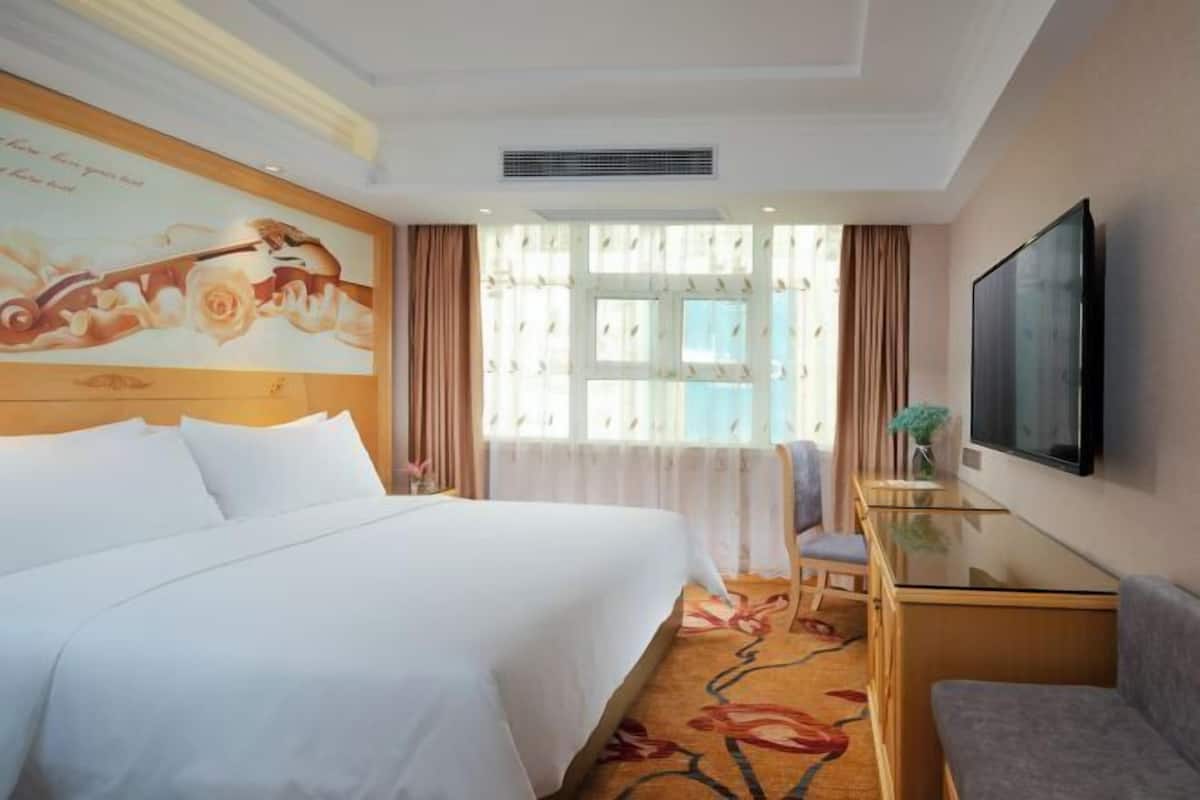 Habitación de hotel con una cama grande, un escritorio, una silla, un televisor y una ventana con cortinas.