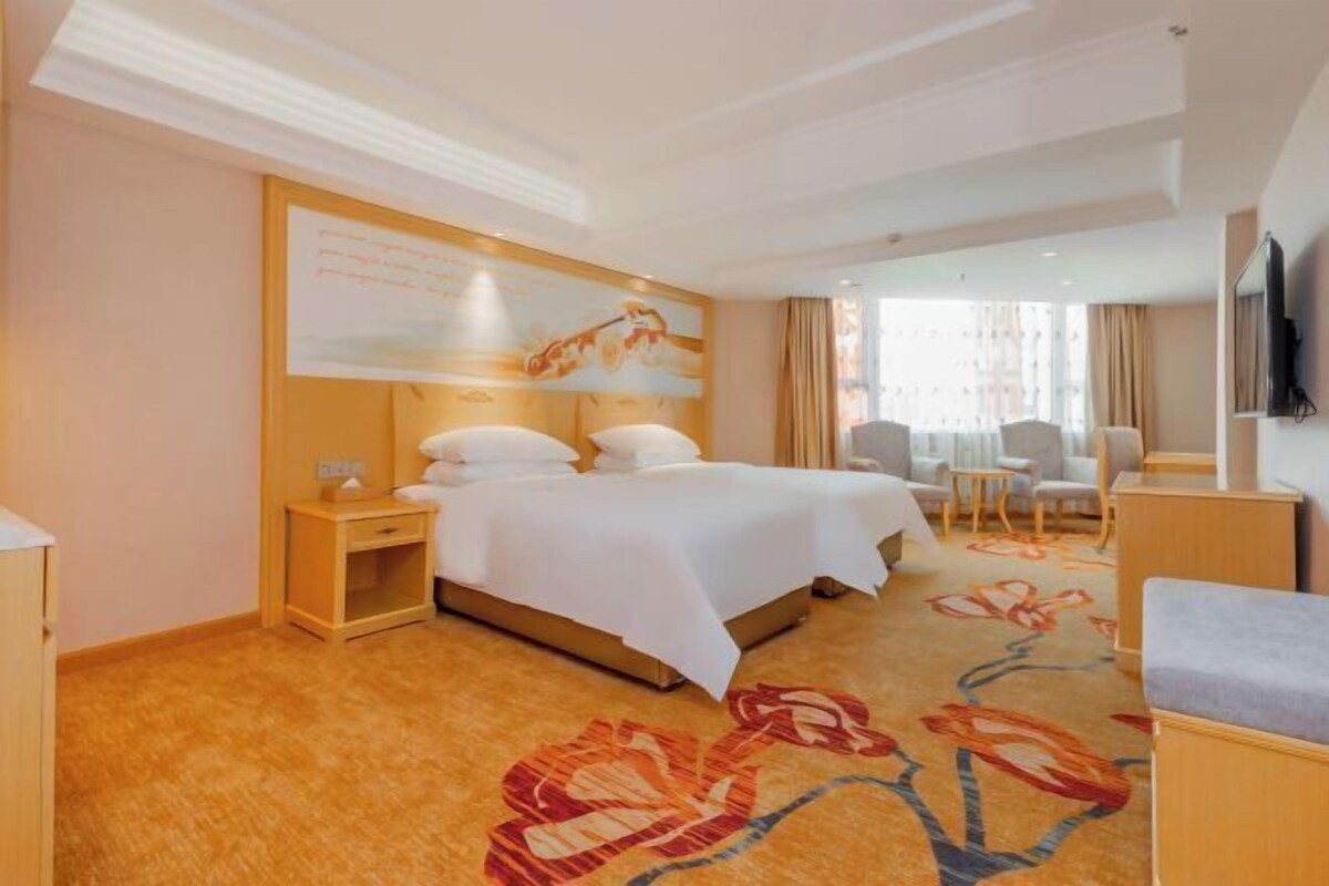 A hotel room with a bed, a desk, a chair, a TV, and a large window.