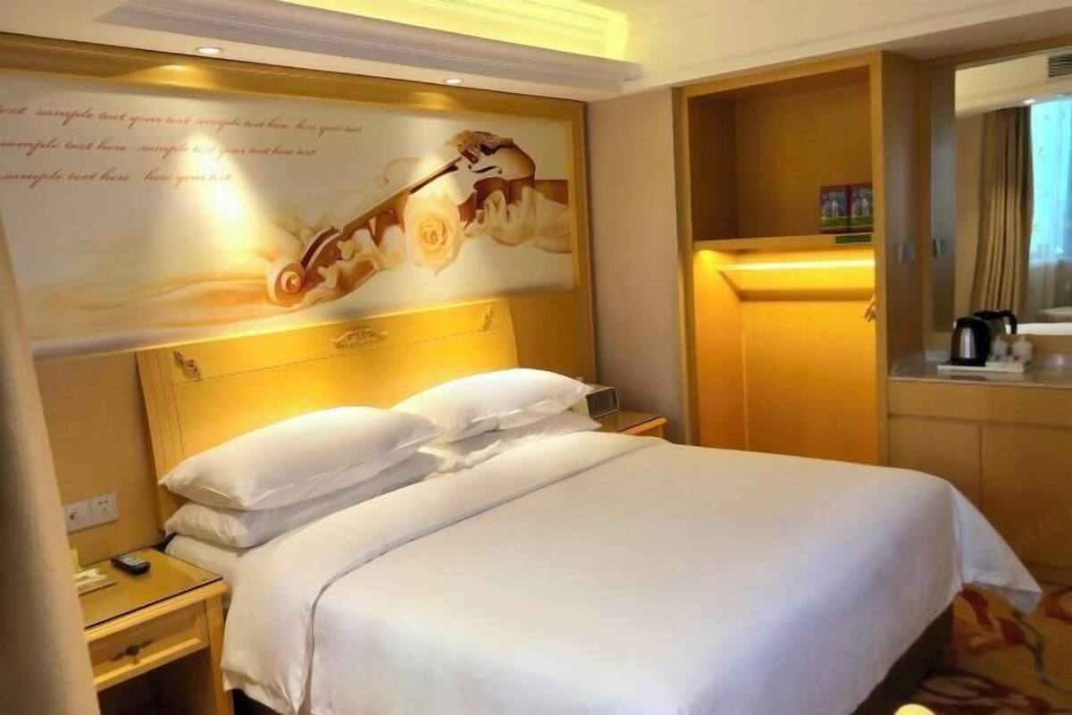 Habitación de hotel con una cama grande, una mesita de noche con lámpara, un espejo y una pared decorada.