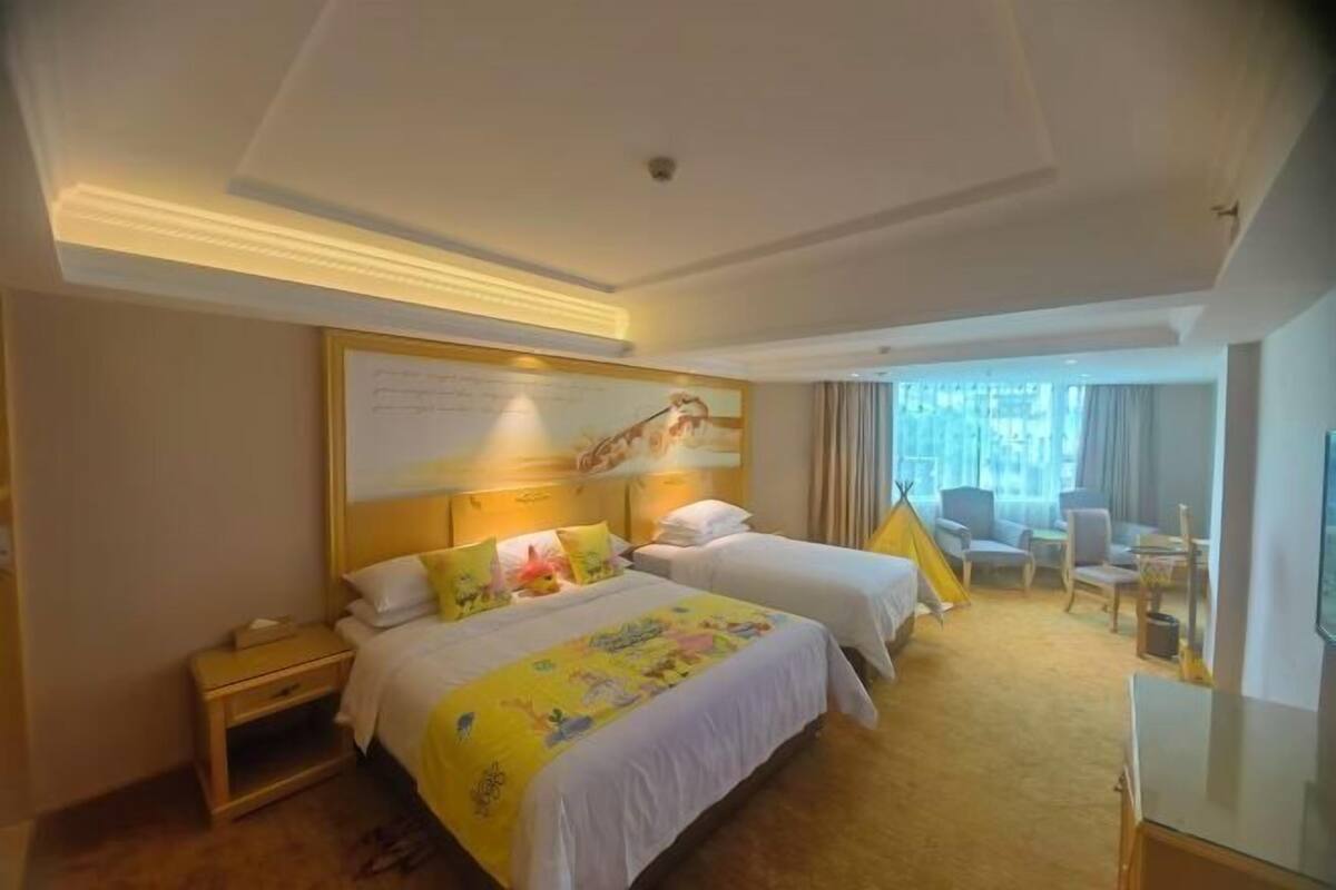 Habitación de hotel con dos camas, un escritorio, una silla y un ventanal con cortinas.