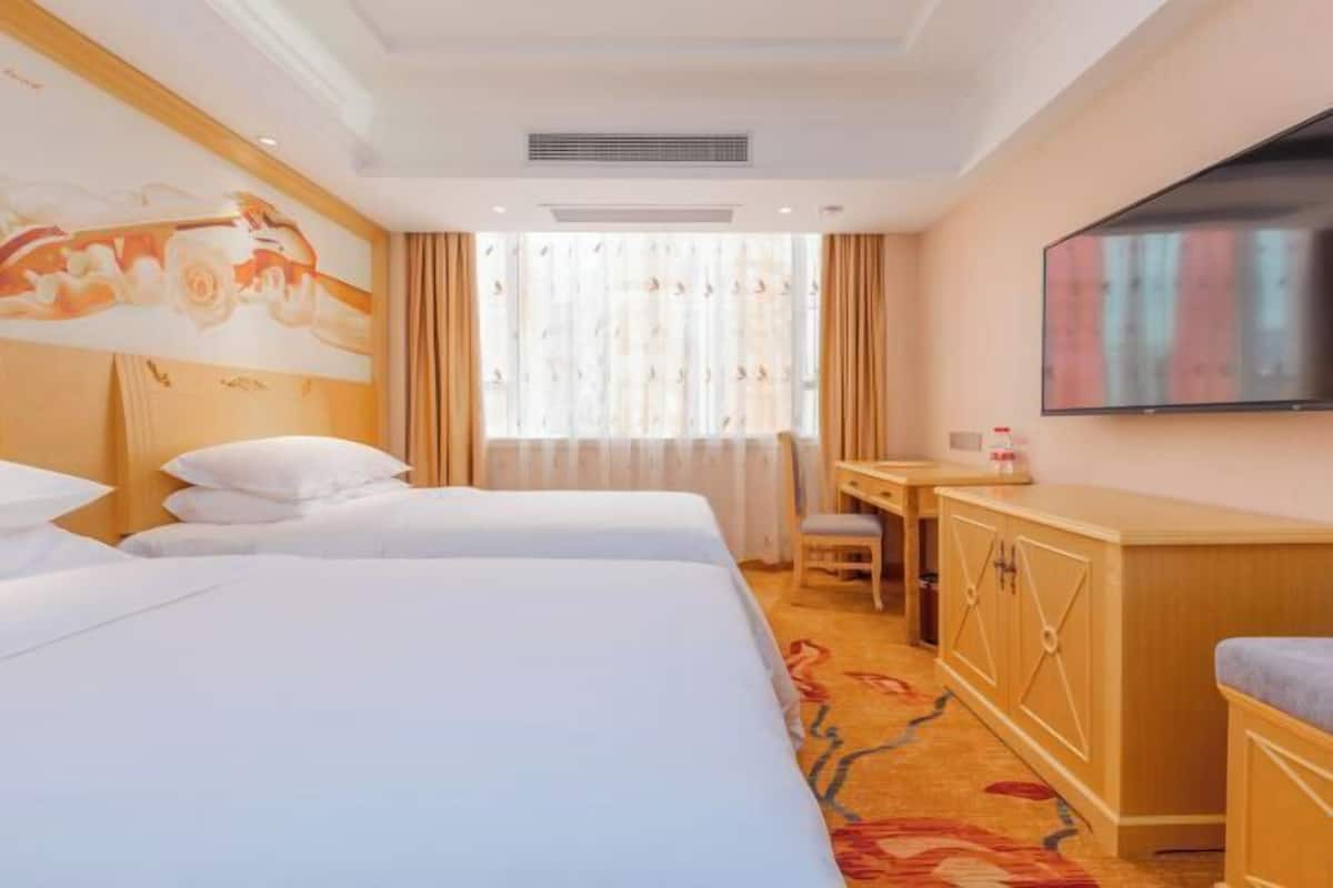 Habitación de hotel con dos camas, un escritorio, una silla, un televisor y una ventana con cortinas.