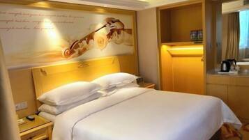 A hotel room with a large bed, a bedside table, a nightstand, a wall-mounted mirror, and a decorative headboard.
