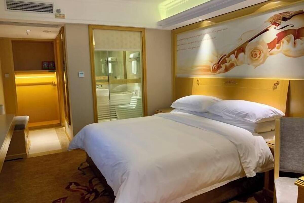 Una habitación de hotel con una cama, un banco, un espejo y una puerta que da a un baño.
