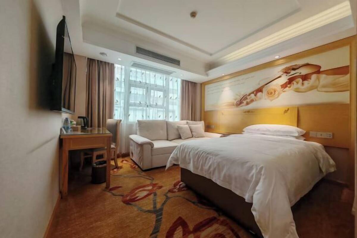 Una habitación de hotel con cama, escritorio, silla, televisor y una ventana grande.