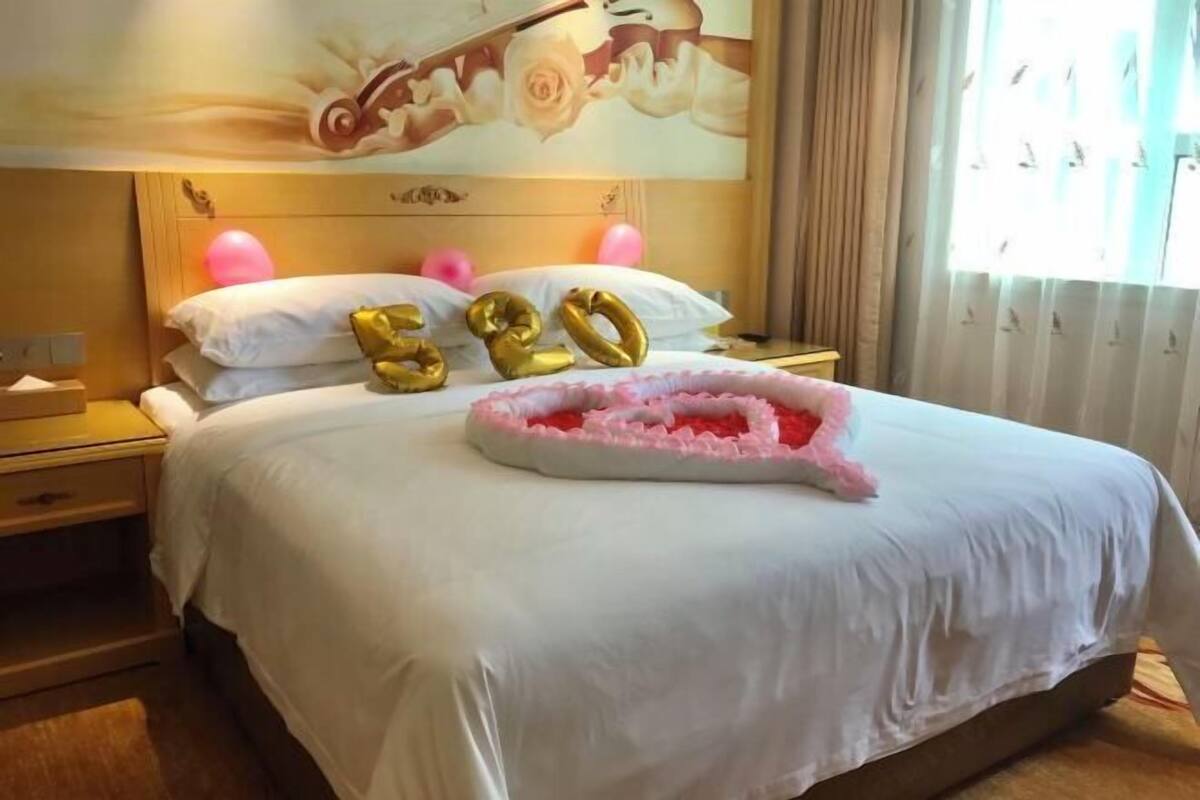 Habitación de hotel con cama, mesita de noche, teléfono fijo en la pared y ventana con cortinas.