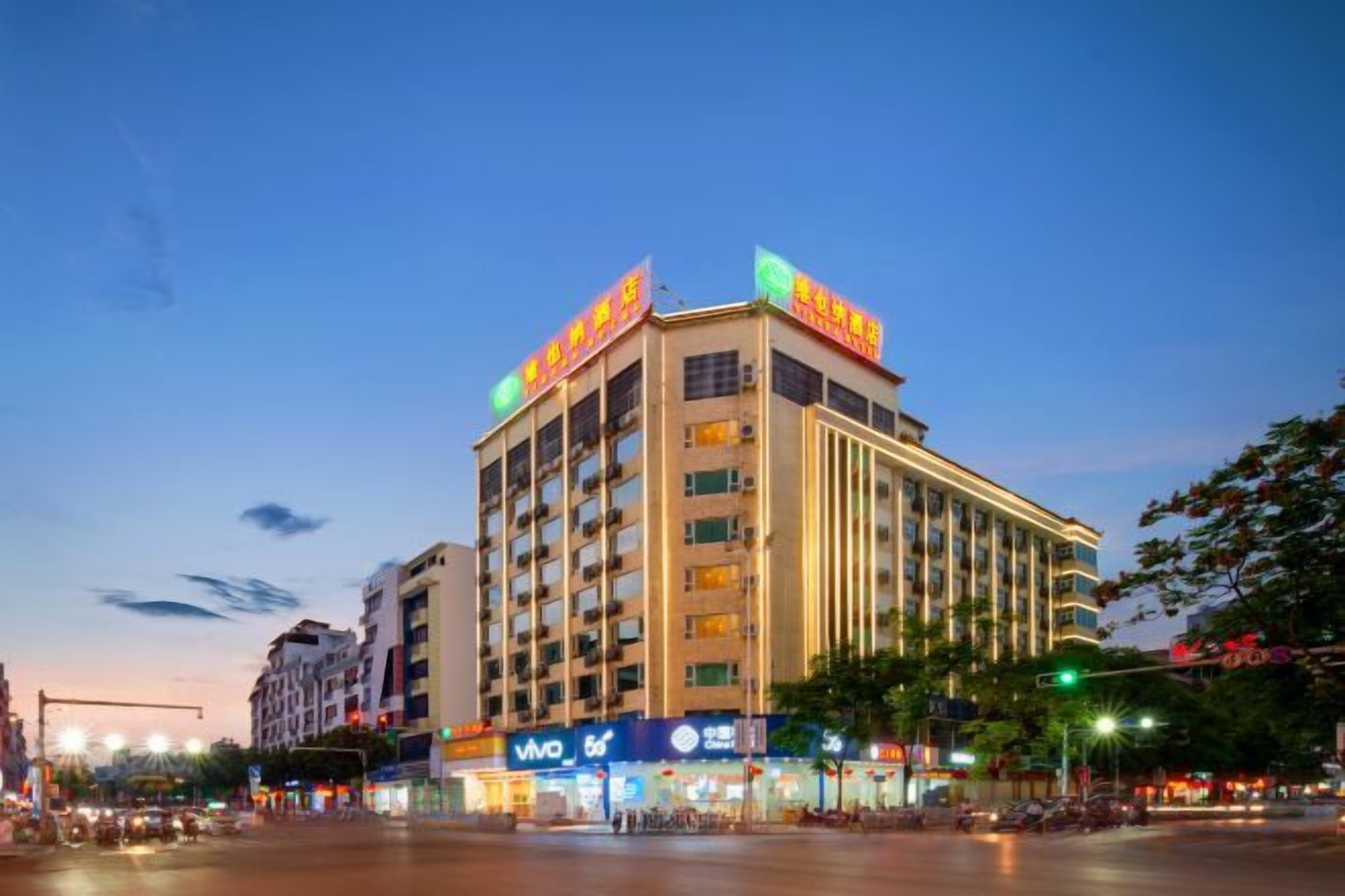 A multi-story hotel with a prominent sign on the top, a large entrance with a ramp, and a busy street in front.