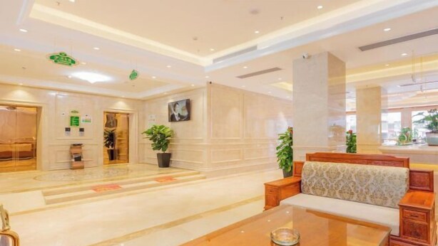 Un vestíbulo amplio con piso de mármol, un mostrador de recepción de madera y una zona de estar con bancos acolchados.