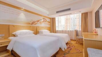A hotel room with two beds, a desk, a chair, a large window with curtains, and a wall with a decorative mural.
