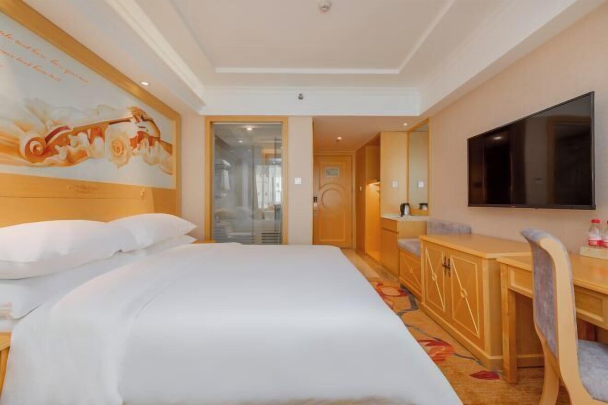 A hotel room with a large bed, a desk, a chair, a flat-screen TV, and a painting on the wall.