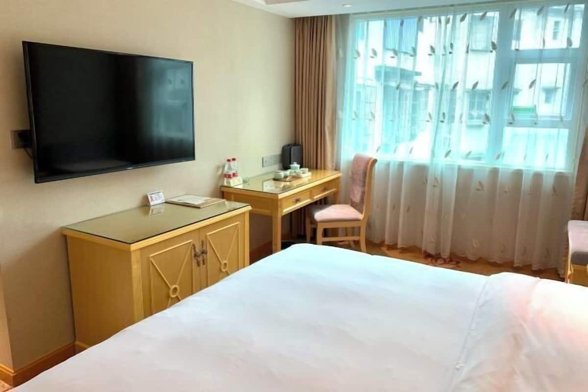 A hotel room with a bed, a desk, a chair, a television, and a window with curtains.