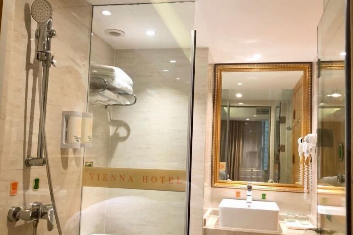 A modern bathroom with a glass shower enclosure, a vanity with a mirror, and a sign indicating the Vienna Hotel.