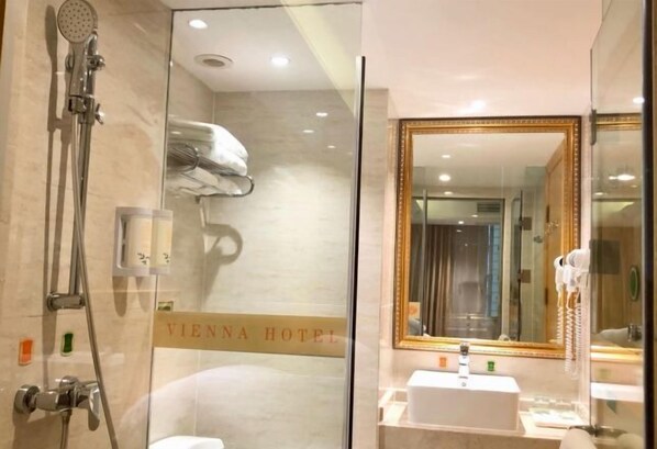 A modern bathroom with a glass shower enclosure, a vanity with a mirror, and a sign indicating the Vienna Hotel.