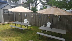A backyard with two picnic tables and two umbrellas, surrounded by a wooden fence.
