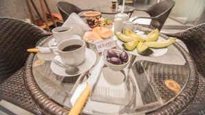 Een ronde glazen tafel met een dienblad waarop koffiekopjes, brood, avocado plakjes en olijven staan.