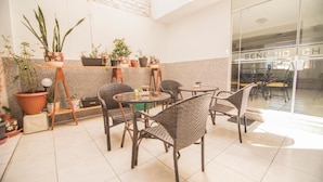 Een zonnig patio met rieten stoelen en tafels, omringd door potplanten.