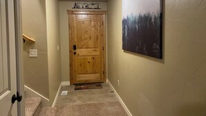 Un corridoio con una porta in legno, un tappetino d'ingresso e un quadro appeso al muro.