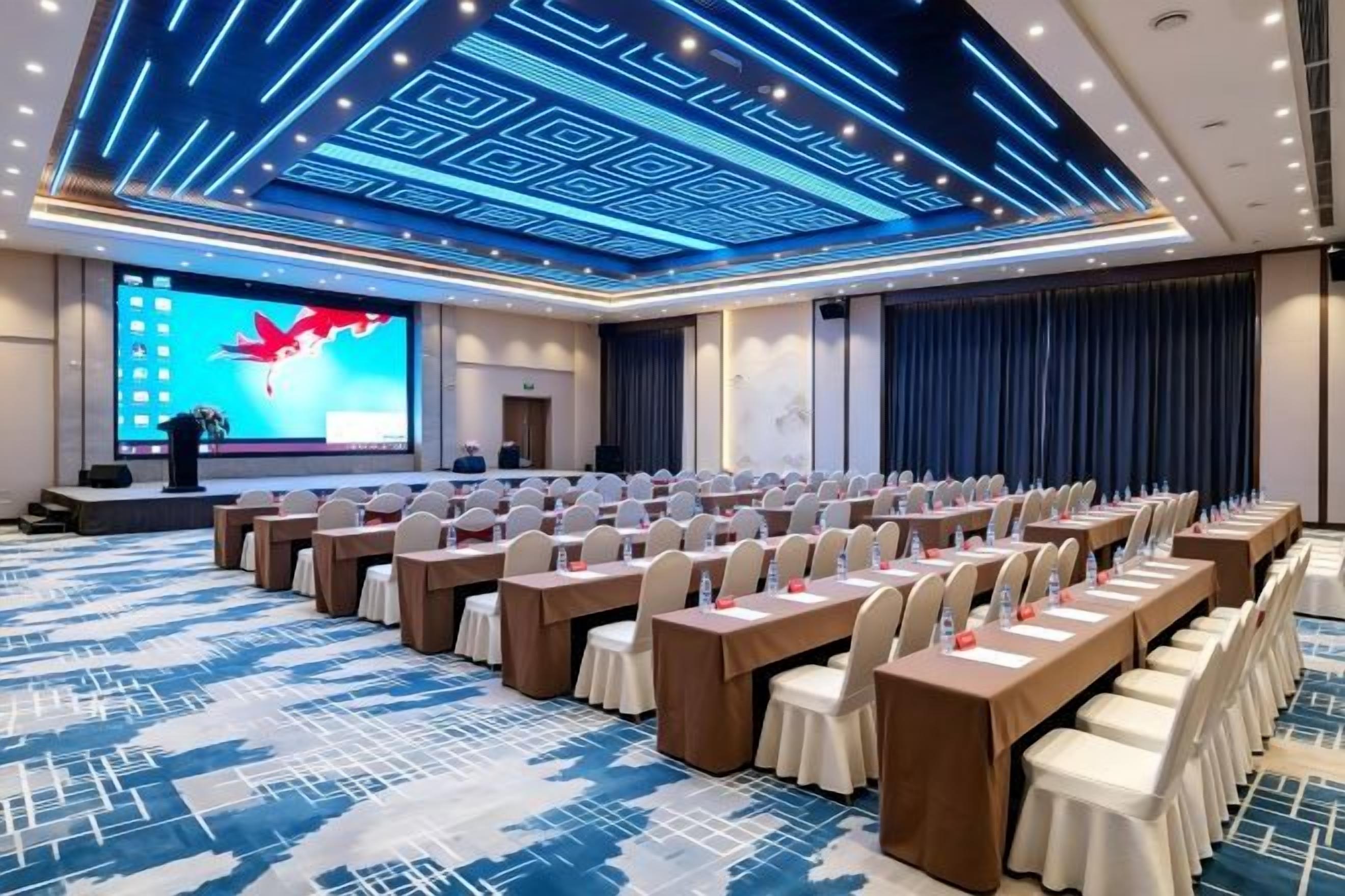 A conference room with rows of tables and chairs, a large screen, and a podium.