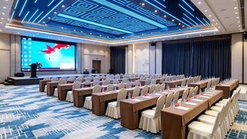 A conference room with rows of tables and chairs, a large screen, and a podium.