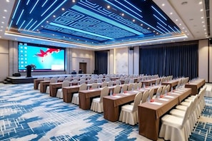 Una sala de conferencias con filas de mesas y sillas, una pantalla grande y un atril.