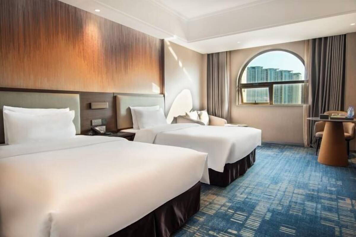 A hotel room with two beds, a round table, and a view of high-rise buildings.