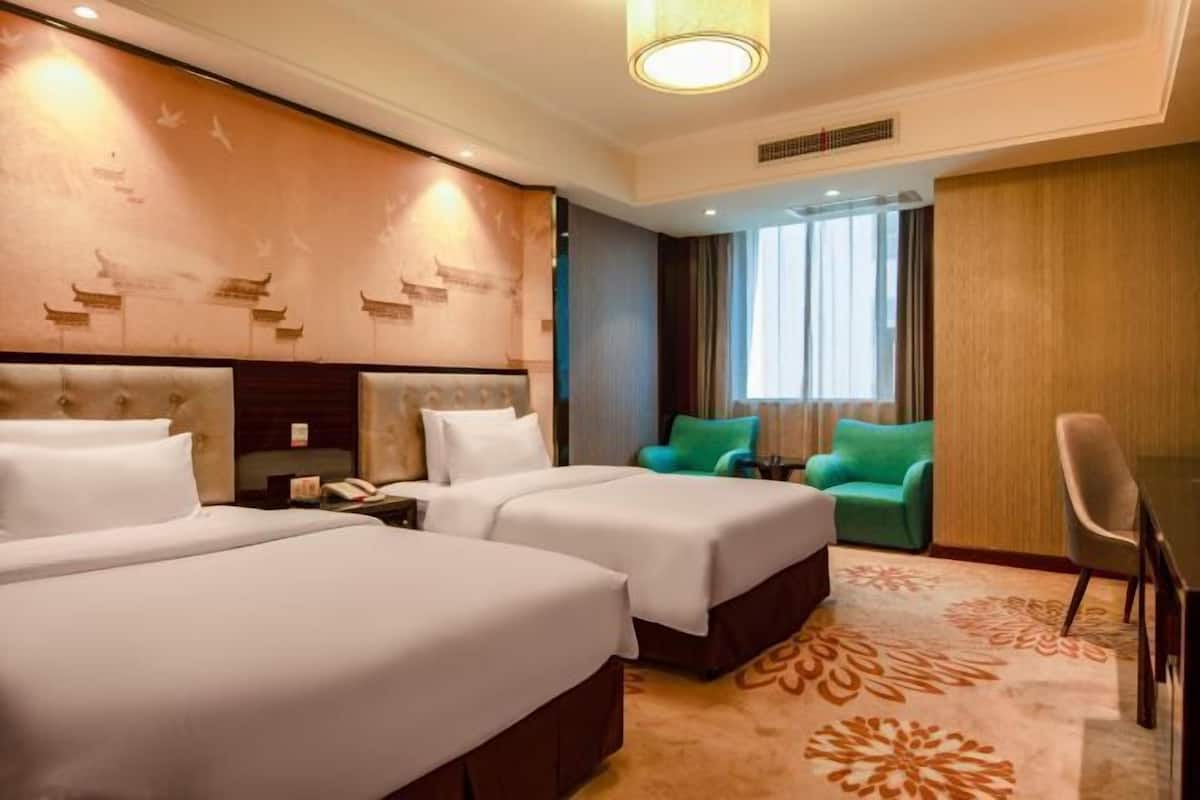 A hotel room with two beds, a desk, a chair, and a window with curtains.
