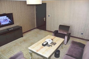 A hotel room with a flat-screen TV on a stand, a coffee table with a remote control, a magazine, and a tissue box. There are two armchairs and a sofa. - Wanjia Oriental Hotel (Jinjiang)