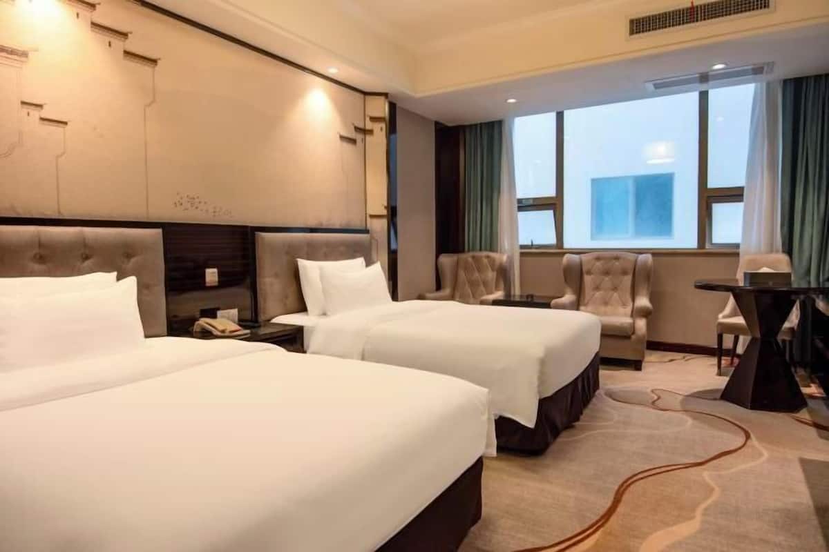 A hotel room with two beds, a chair, a table, and a window with curtains.