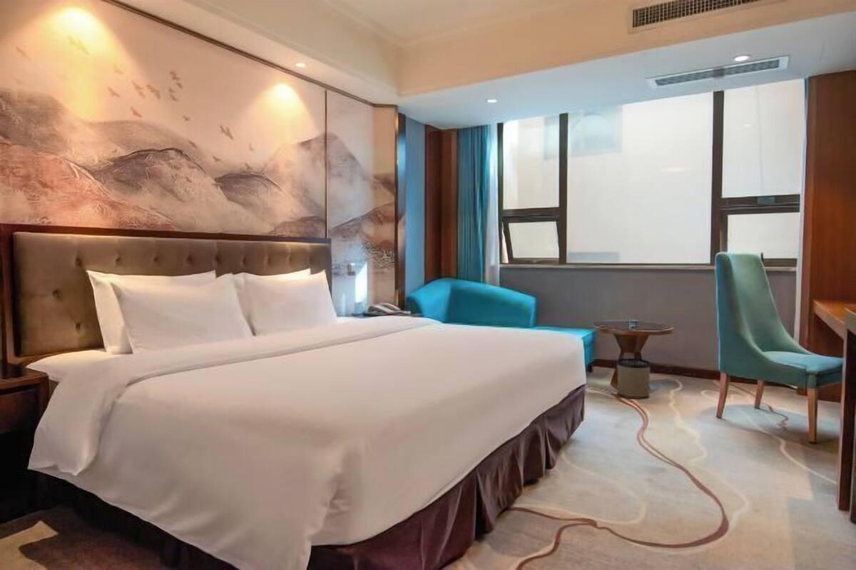 A hotel room with a large bed, a desk, a chair, and a view of the city.