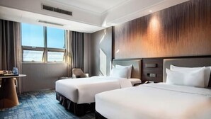 Habitación de hotel con dos camas, un escritorio y vista al mar.