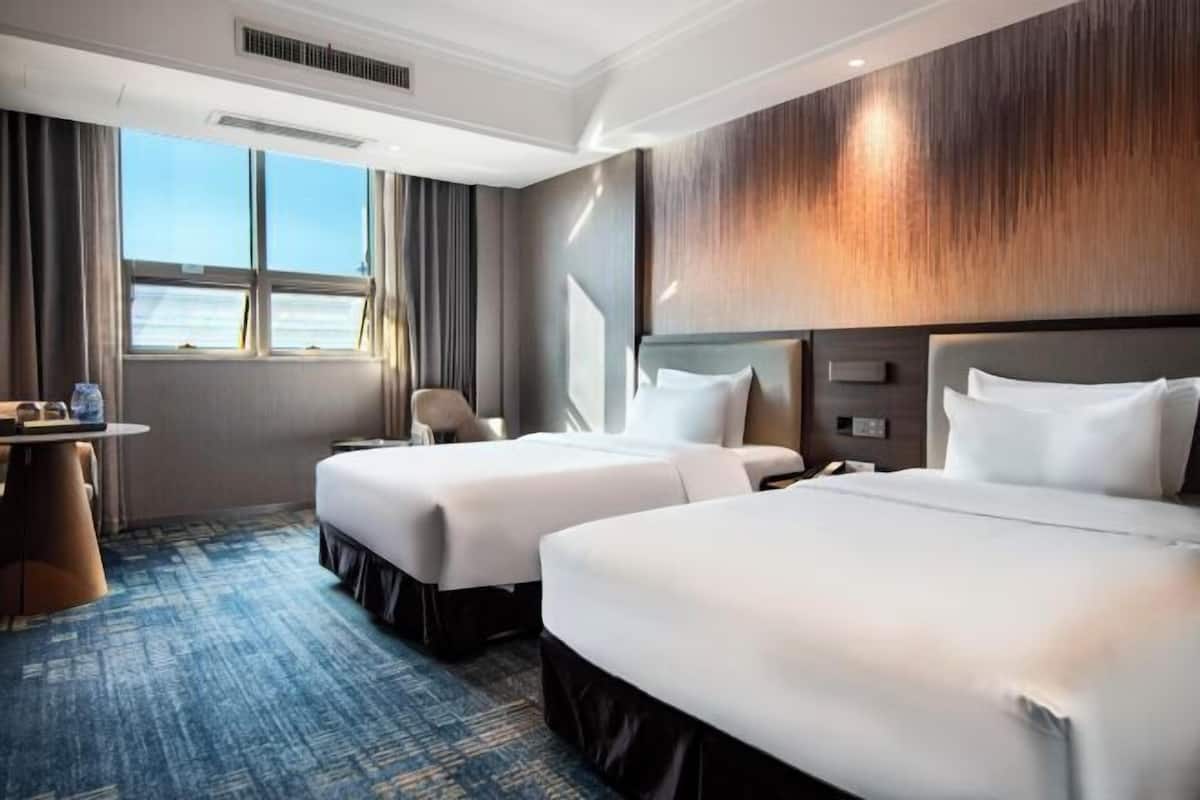 A hotel room with two beds, a desk, and a view of the sea.