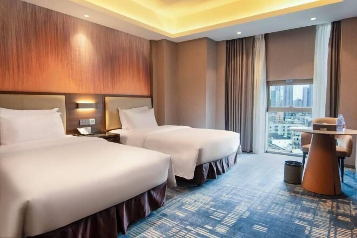 A hotel room with two beds, a small table, and a view of the city.