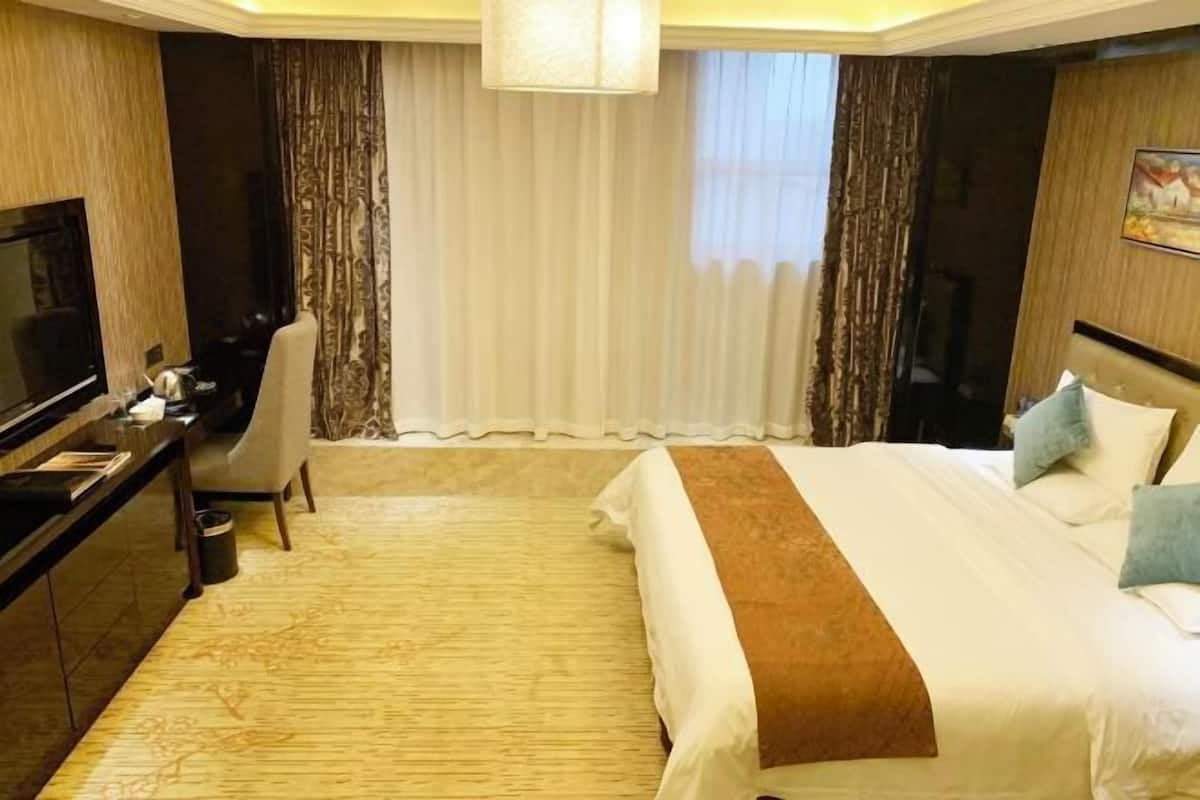 A hotel room with a large bed, a desk with a TV, a chair, and a window with curtains.