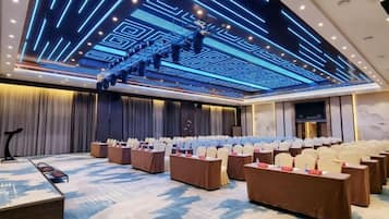 A conference room with a stage, rows of tables, and chairs, and a ceiling with a geometric light design.