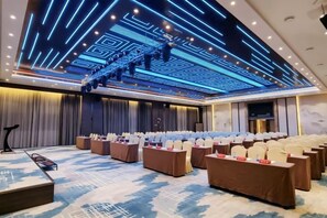 A conference room with a stage, rows of tables, and chairs, and a ceiling with a geometric light design. - Wanjia Oriental Hotel (Jinjiang)