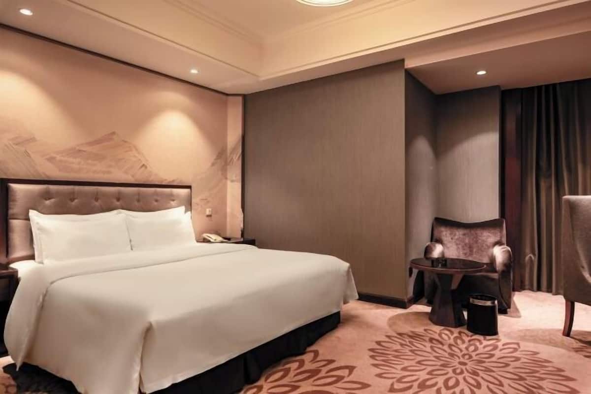 A hotel room with a large bed, a small table, a chair, and a decorative rug.